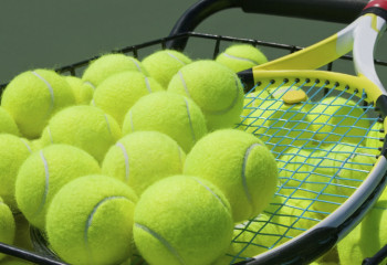 Close up of tennis balls in a basket with a raquet.
