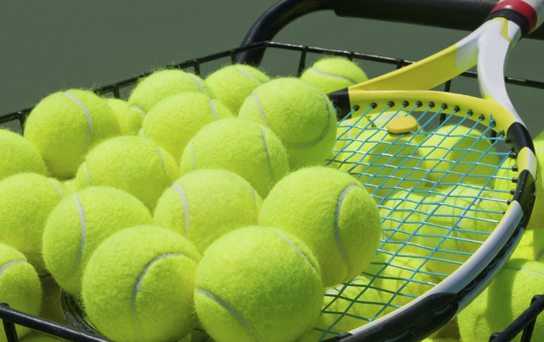 Close up of tennis balls in a basket with a raquet.